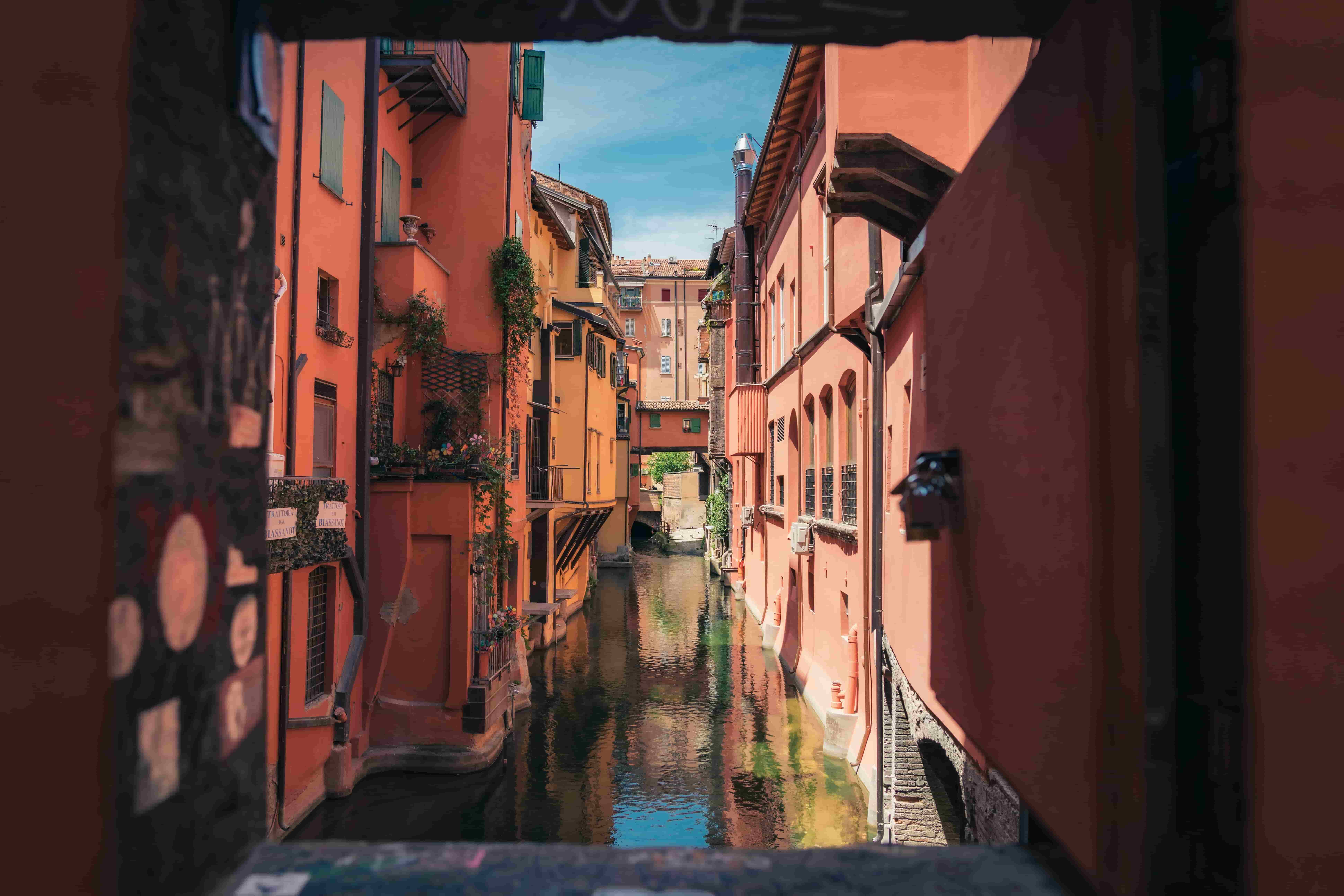 Una vista affascinante del canale segreto di Bologna attraverso la Finestrella di Via Piella. La piccola finestra incornicia un pittoresco corso d’acqua, con vecchi edifici riflessi nell'acqua e edera verde che aggiunge un tocco romantico.