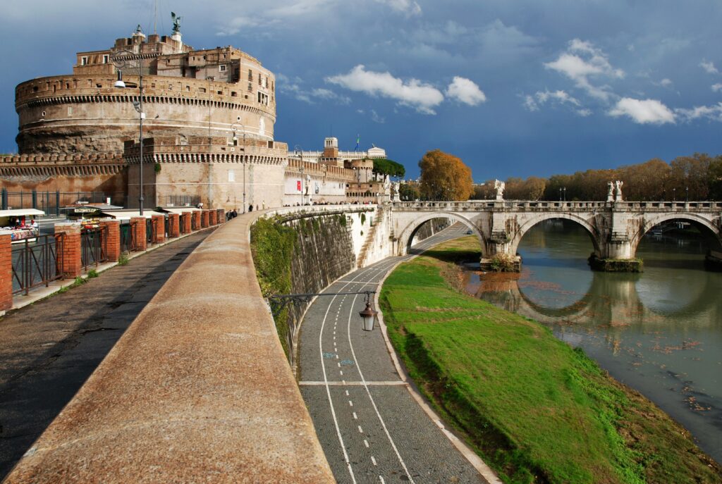 Historic Castel Sant'Angelo in Rome overlooking the Tiber River and bridge under a dramatic sky.