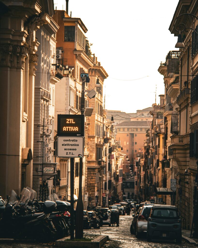 Picturesque street in Italy lined with classic architecture, motor scooters, and cars at sunset.
