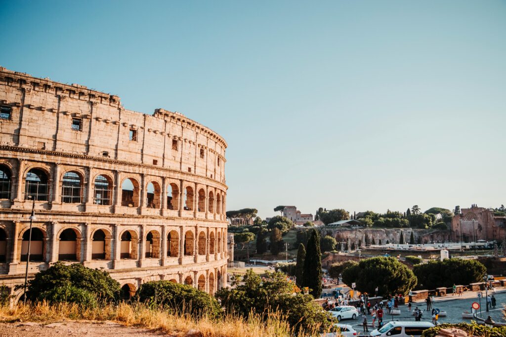 The iconic Colosseum in Rome, a historic amphitheater surrounded by urban scenery on a bright day.