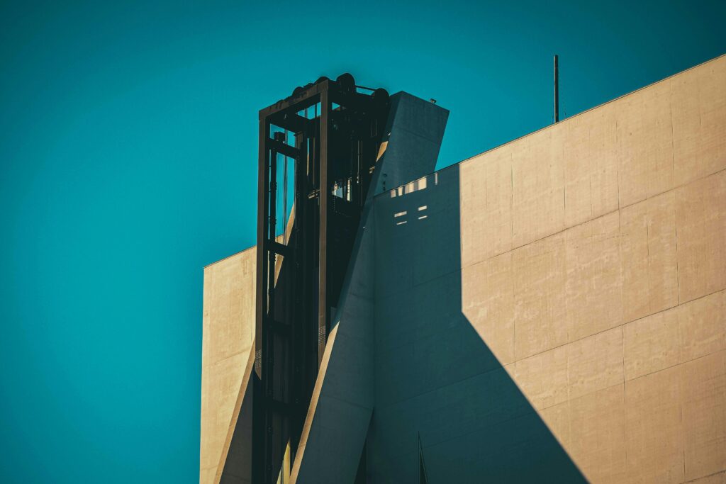 From below exterior fragment of contemporary Fondazione Prada museum building with geometric shapes and outdoor elevator against cloudless blue sky in Milan