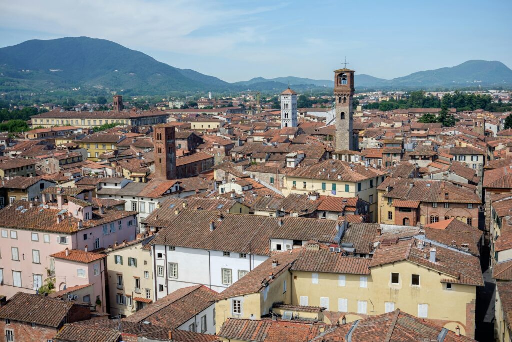 Explore the charming rooftops and towers of historic Lucca, Italy, set against a backdrop of scenic Tuscan mountains.