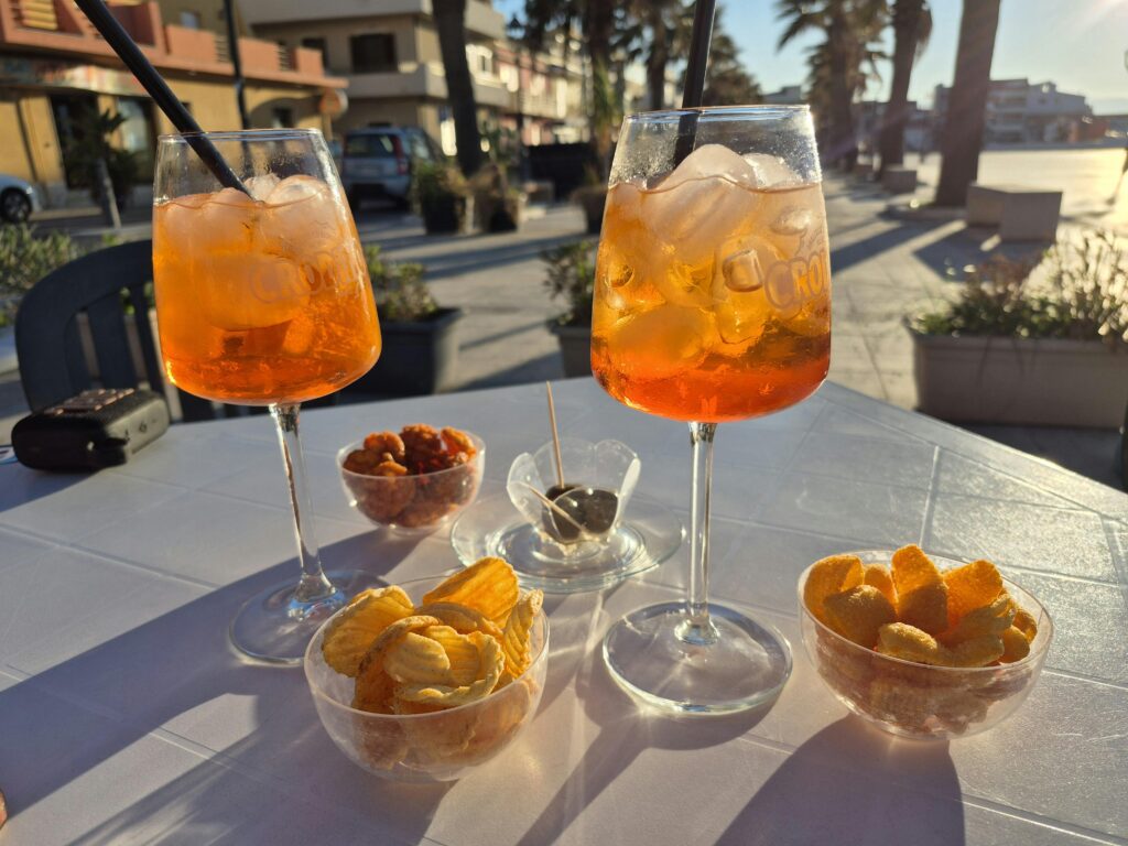Savoring Aperol Spritz with snacks at a sunny outdoor café in Calderà, Sicily.