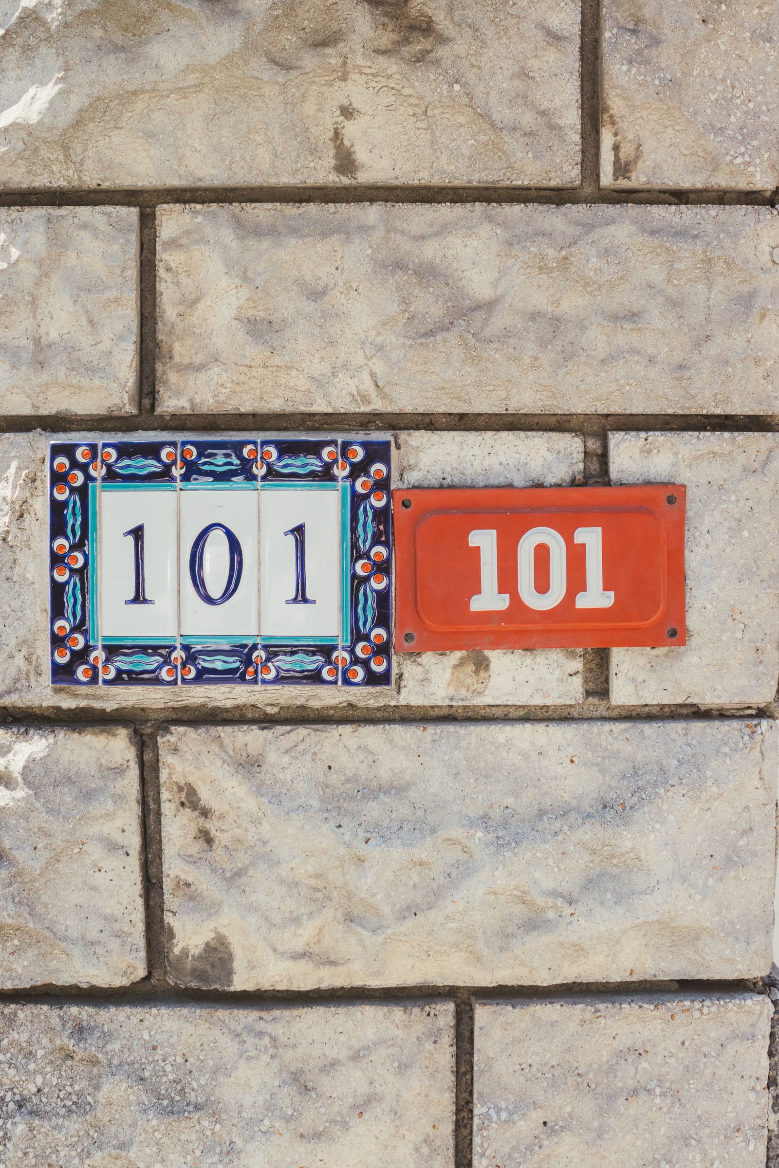Ceramic tiles showing the house number 101 mounted on a textured stone wall