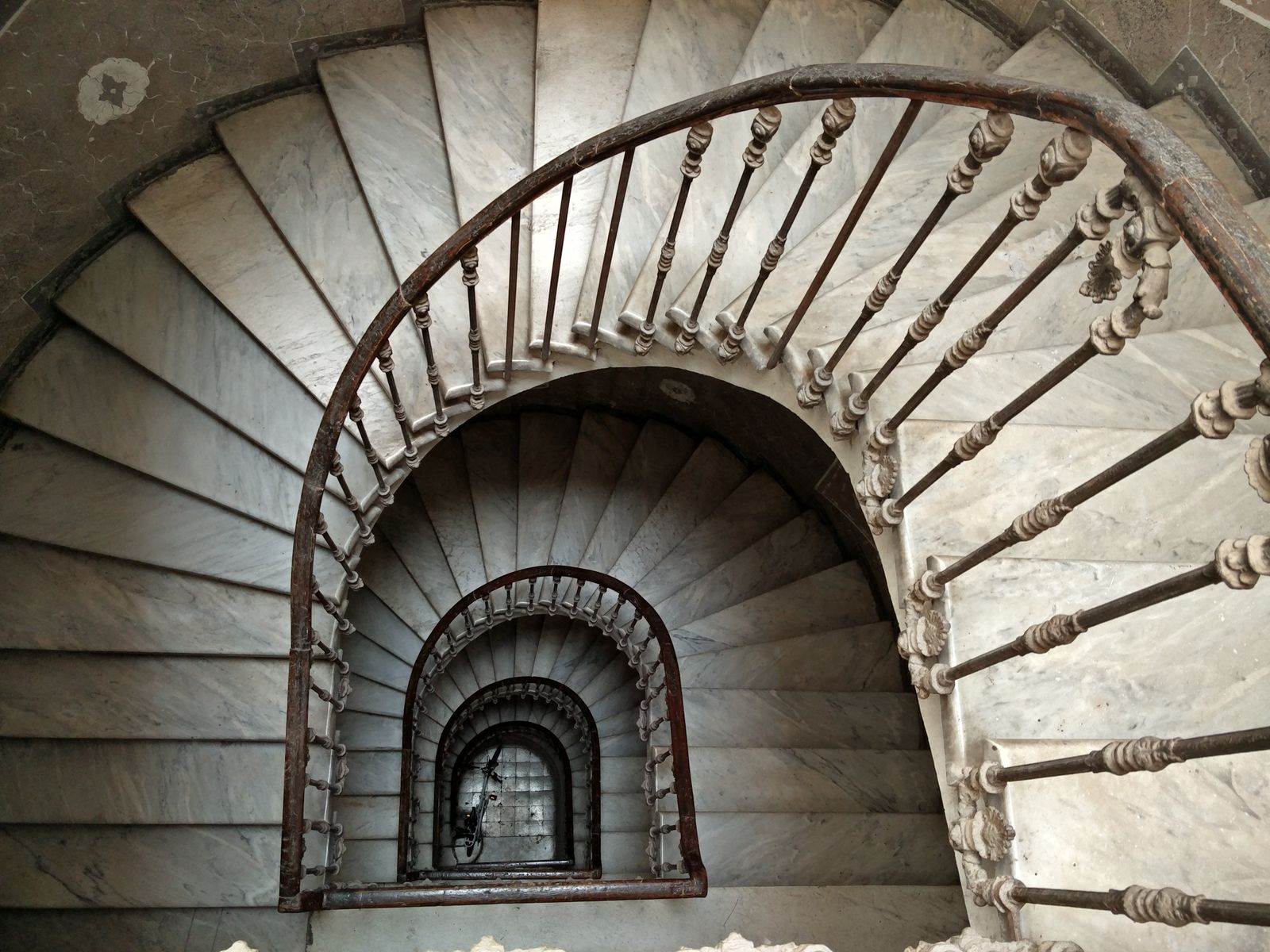 Marble spiral staircase winding upward through the stairwell of an old building in Rome