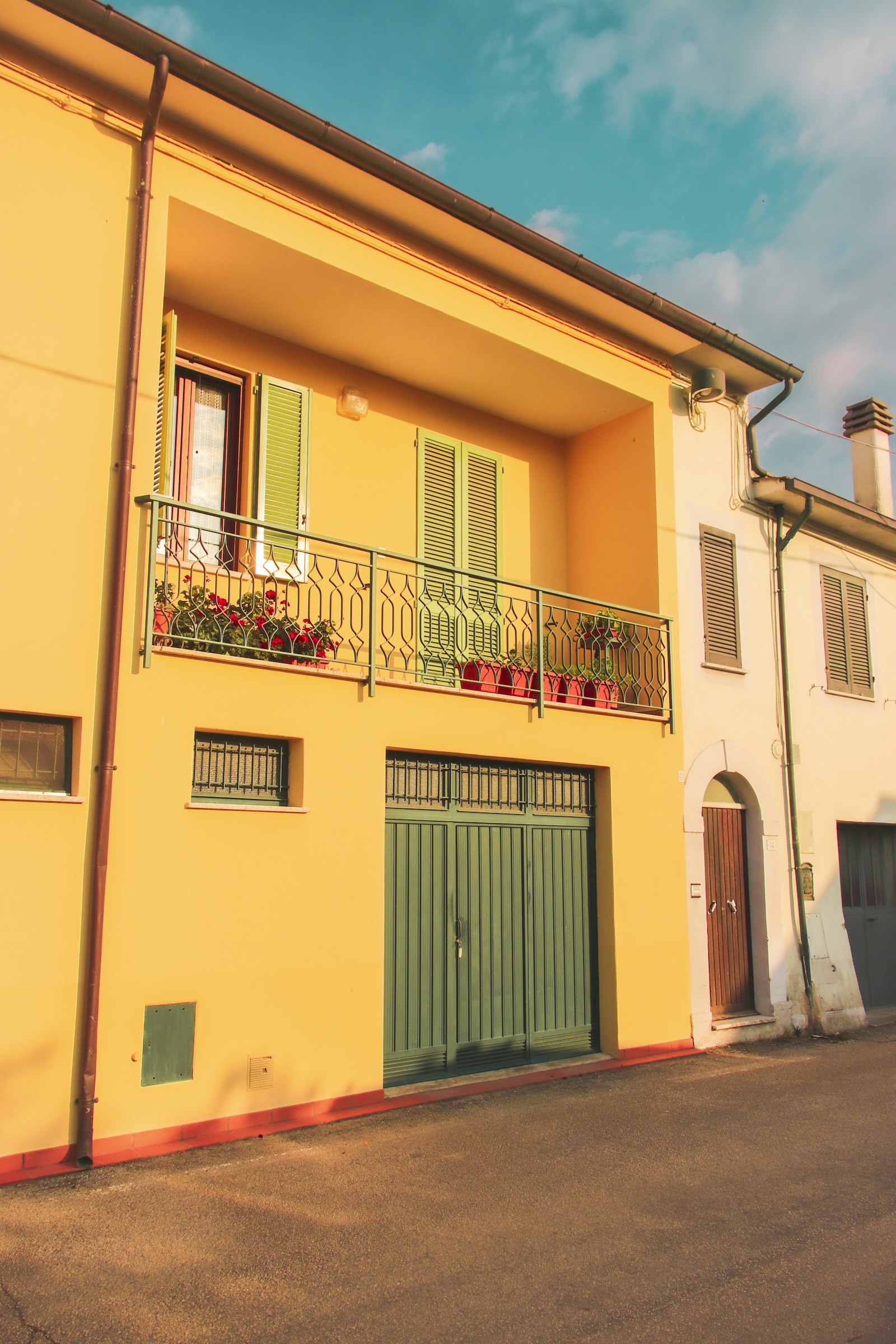 Yellow Italian building with green louvered persiane shutters and a small balcony