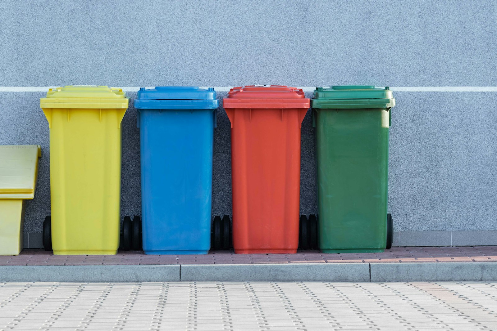 Four different coloured waste separation bins standing beside a wall