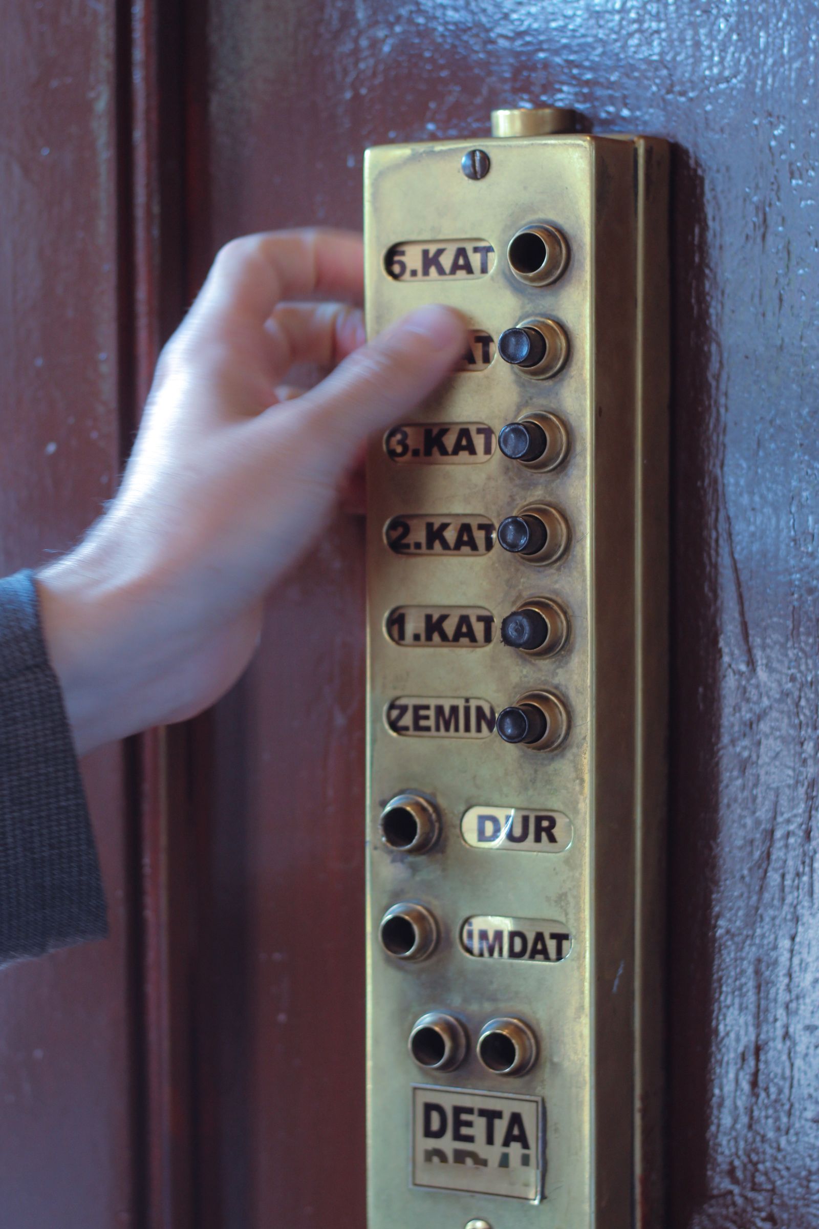 Hand pressing a floor button on an old-fashioned lift control panel with numbered buttons