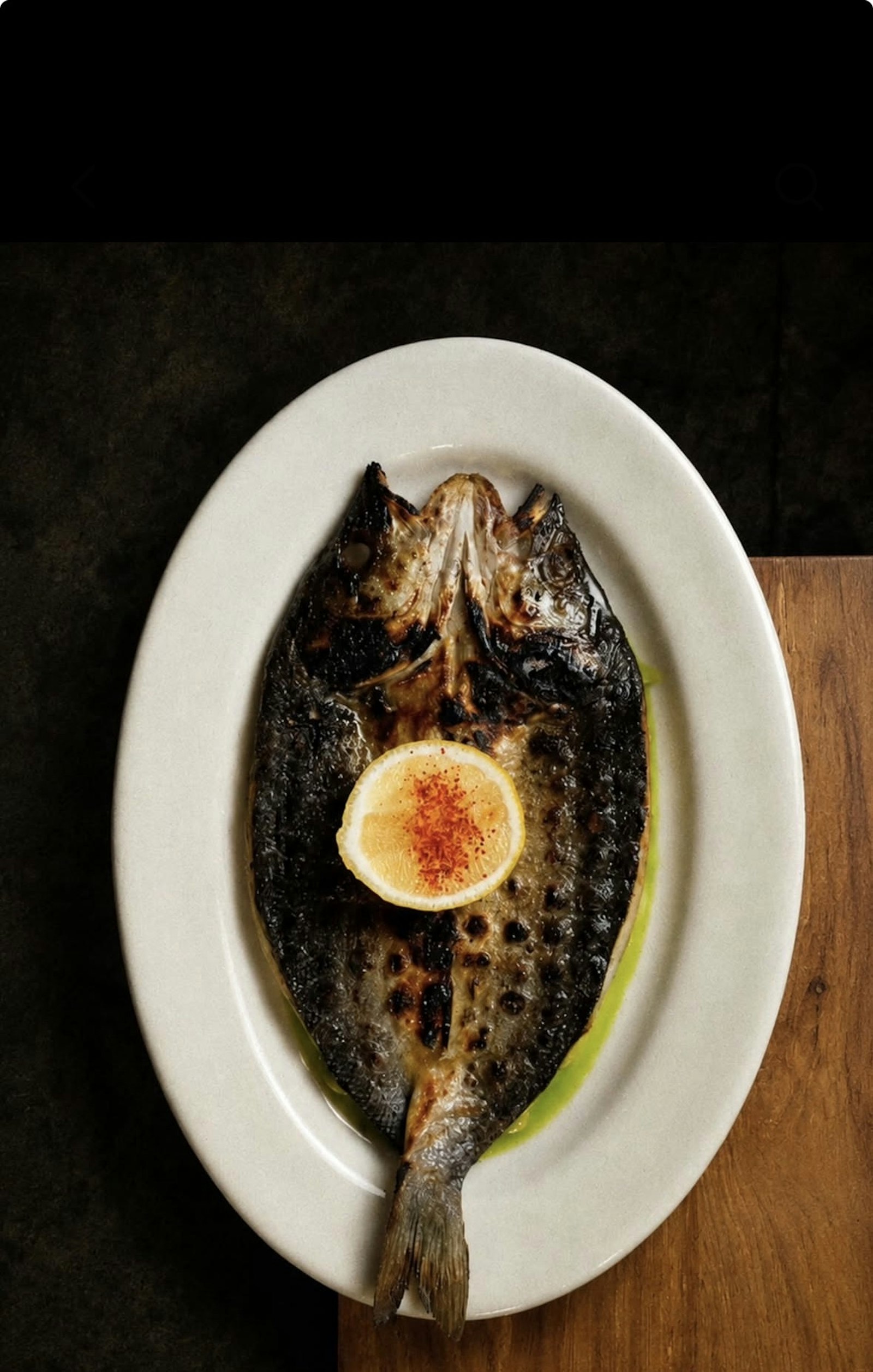 Whole grilled fish served with lemon on a white plate