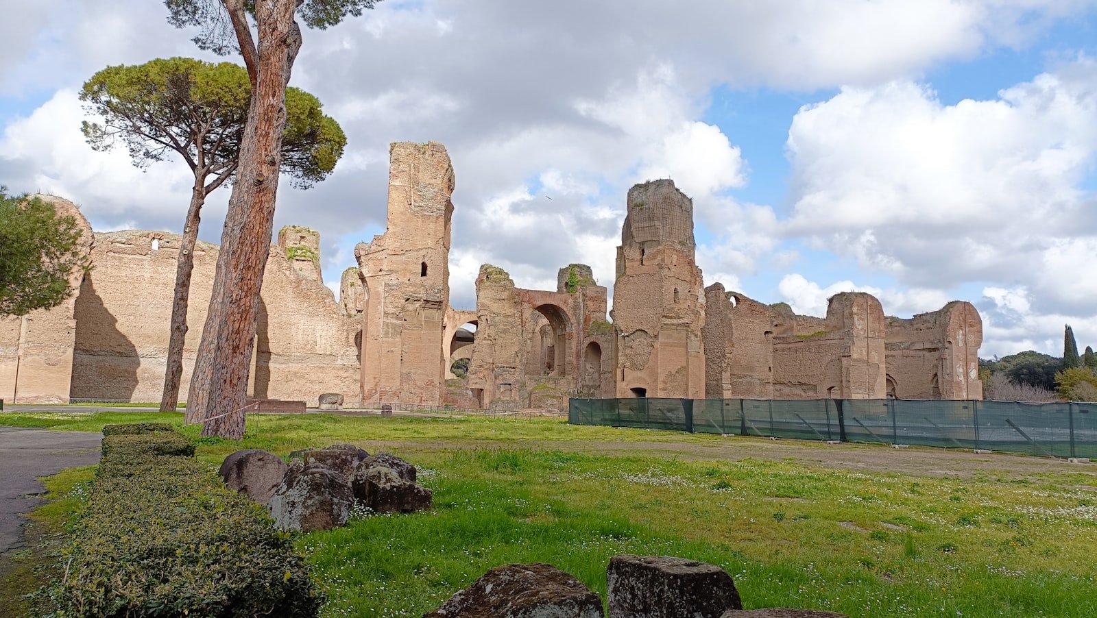 Tall brick walls of the Baths of Caracalla ruins in Rome behind grass and umbrella pines