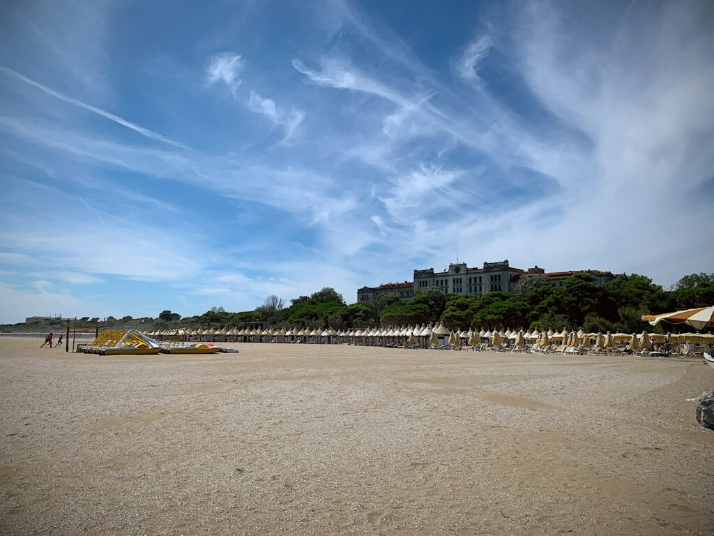 Wide sandy beach on the Venice Lido with rows of beach huts and a large hotel behind