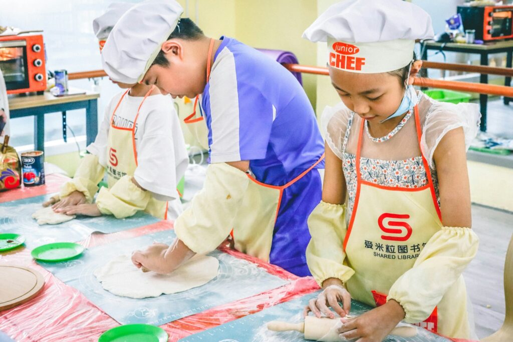 Children in aprons making pizza dough at a cooking class