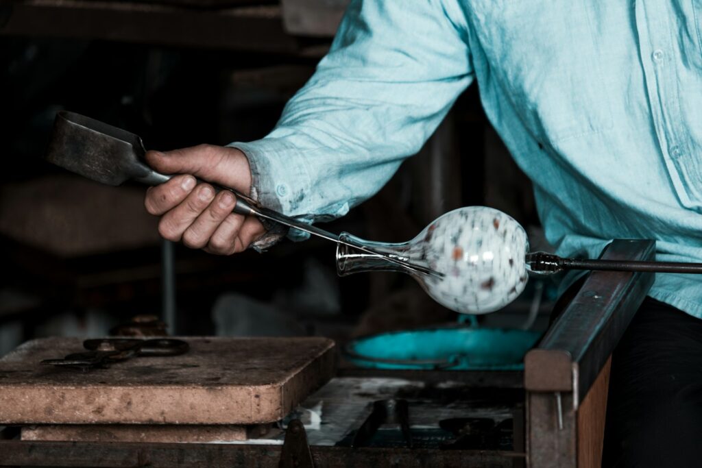 Glassmaker shaping molten glass with tongs