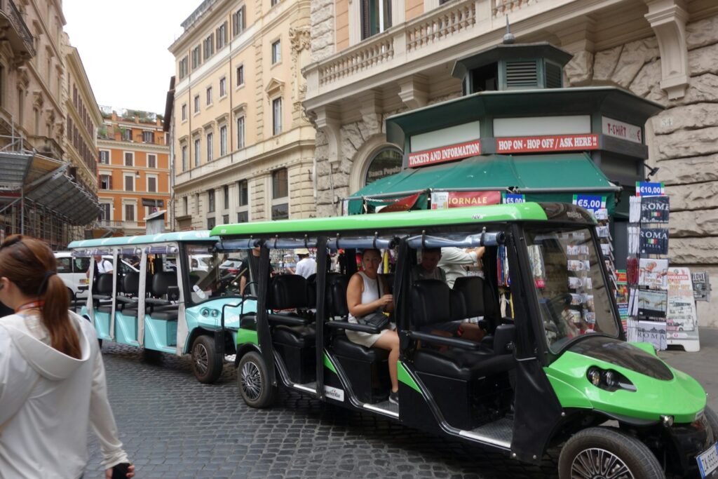 Tourists riding in open-air electric carts on a cobbled street in Rome